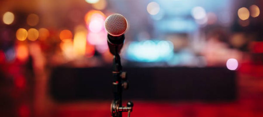 MIC ON A STAGE READY FOR THE SINGER OR SPEAKER WITH BLURRED BCKGROUND AND COLOUR BACK.